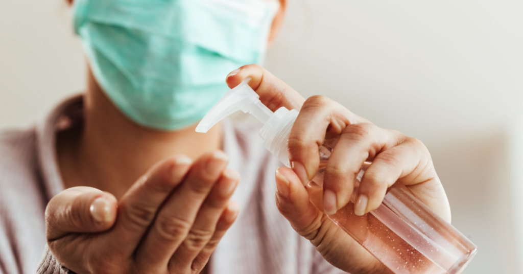 A person wearing a face mask and applying hand sanitizer, emphasizing hygiene and prevention of the common cold and flu.