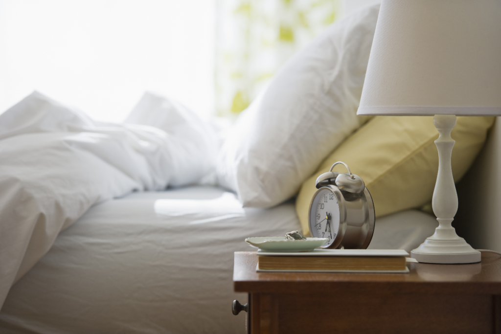 A peaceful bedside setup with a lamp, clock, and book, illustrating a calming environment for winding down before sleep.