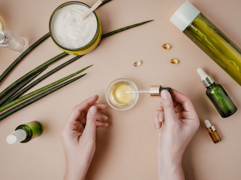 Hands using a dropper with natural skincare products like aloe vera, serums, and oils for gentle skincare routines to manage hormonal acne in women.