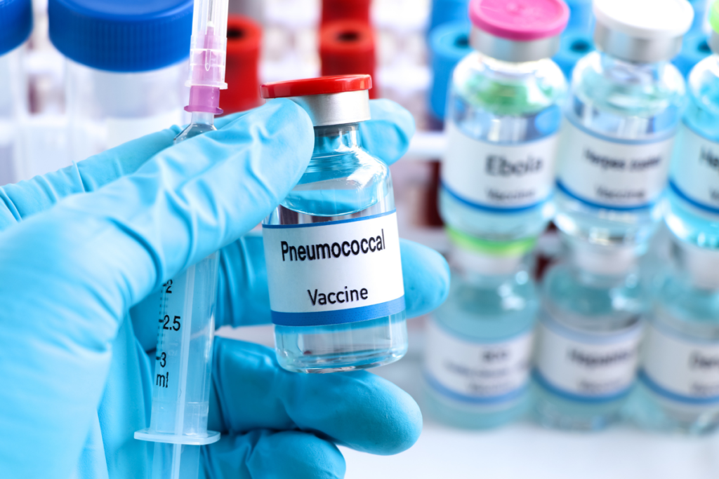 Pneumococcal vaccine vial held by a healthcare provider wearing gloves, with other vaccine vials in the background.