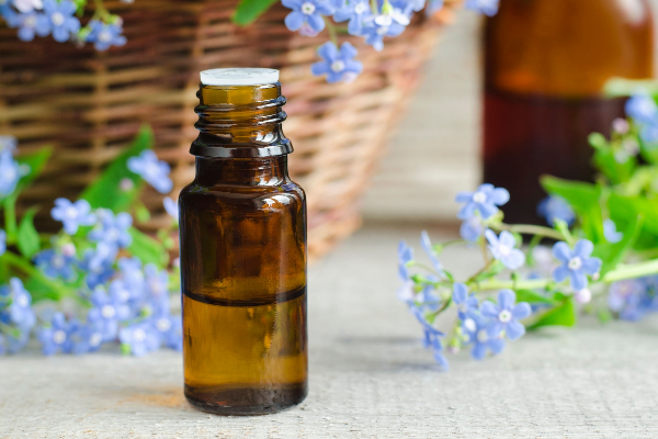 Bottle of essential oil surrounded by fresh flowers, representing natural remedies like rosemary and lavender oil for hair loss.