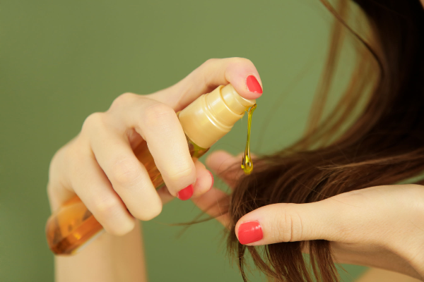 Close-up of hands applying nourishing oil to hair tips, promoting healthy hair care practices.