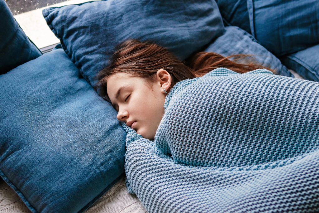 A young woman peacefully sleeping on a cozy bed surrounded by soft pillows, showcasing the importance of restful sleep for mental health.