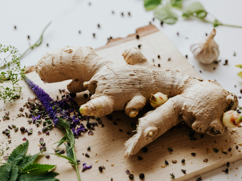 Close-up of ginger root with scattered herbs and flowers on a wooden board, symbolizing natural remedies for liver detox.