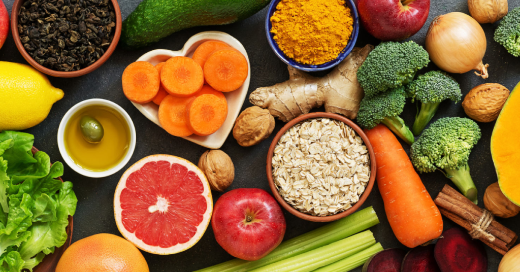 An assortment of detox-friendly foods including carrots, grapefruit, turmeric, broccoli, ginger, oats, and leafy greens, supporting liver health and women's wellness.