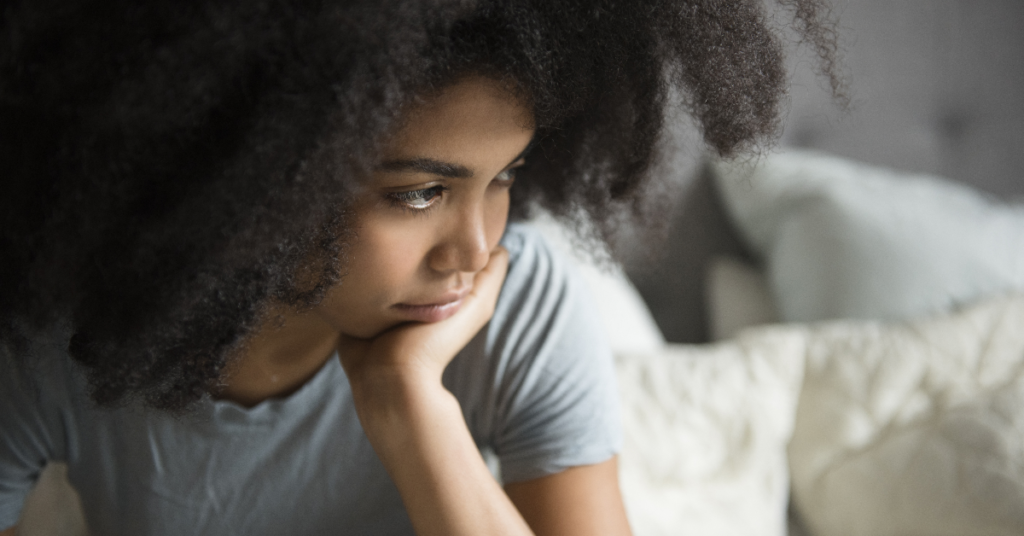 A thoughtful woman sitting on a bed, reflecting signs of anxiety symptoms in women.