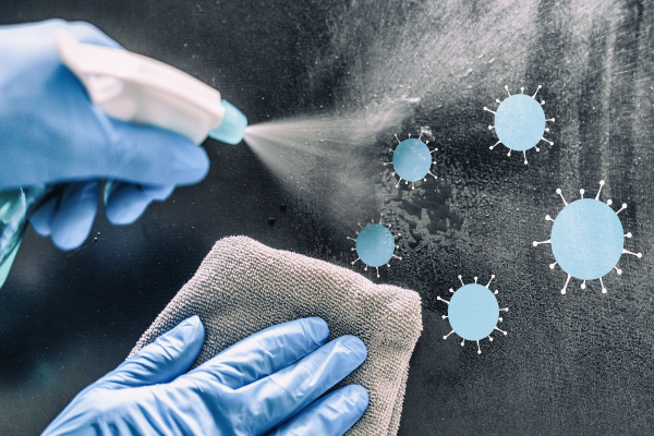 Gloved hands cleaning a surface with disinfectant spray to prevent norovirus.