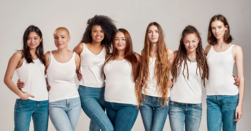 A diverse group of women standing together, wearing casual white tops and jeans, celebrating body positivity and self-acceptance.