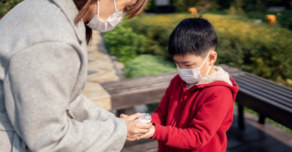 A parent helping a child sanitize hands outdoors, promoting hygiene for norovirus prevention.