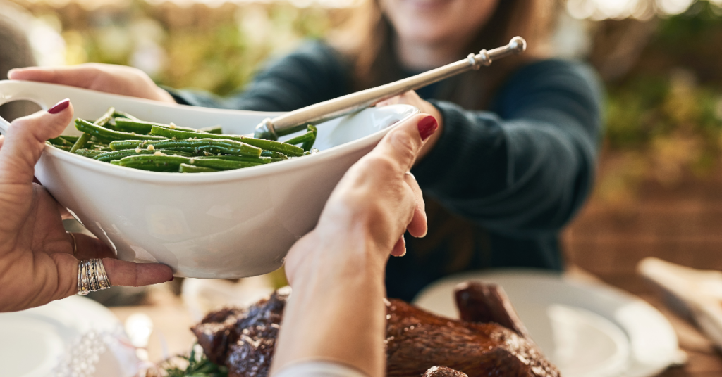 A close-up of women passing a bowl of green beans at a shared meal, reflecting intuitive and mindful eating practices.