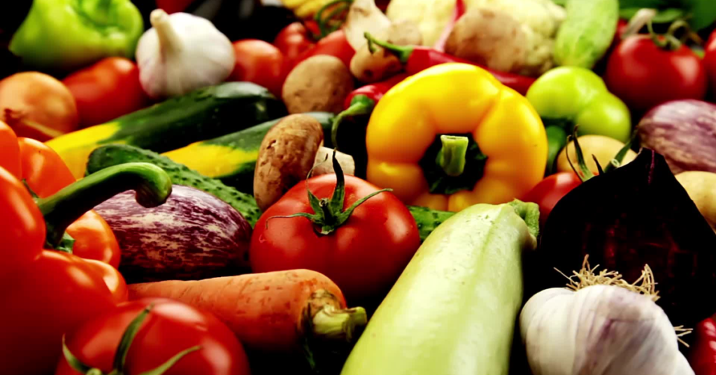 A variety of fresh vegetables including tomatoes, bell peppers, carrots, zucchini, garlic, and eggplant, rich in vitamins and iron for anemia management.