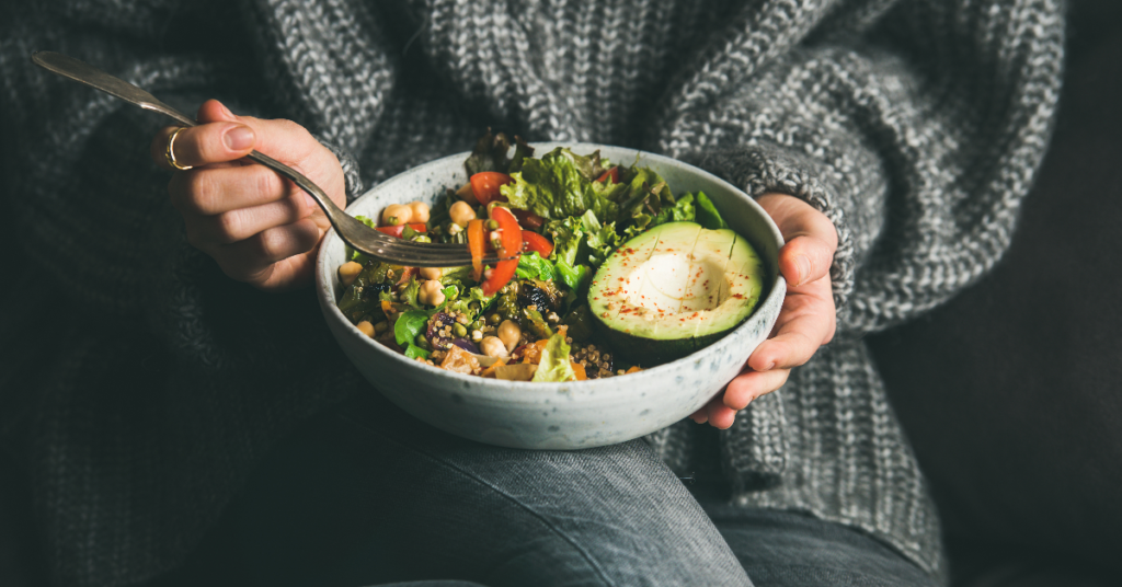 Close-up of a woman holding a bowl of salad with fresh avocado, chickpeas, and greens, reflecting mindful and healthy eating.