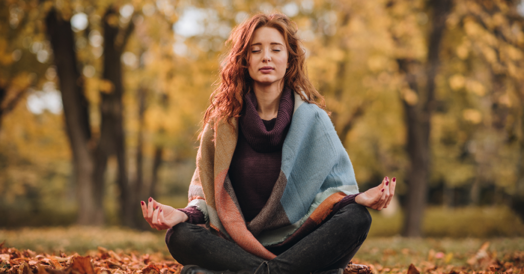 A woman meditating outdoors in an autumn setting, highlighting relaxation and mindfulness.