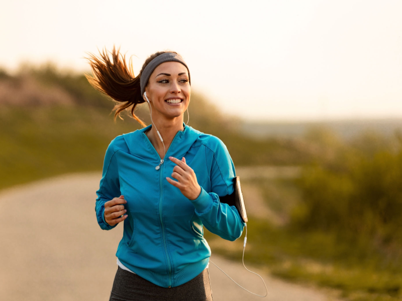 Smiling woman jogging outdoors, showcasing cardio as a way to balance hormones naturally.