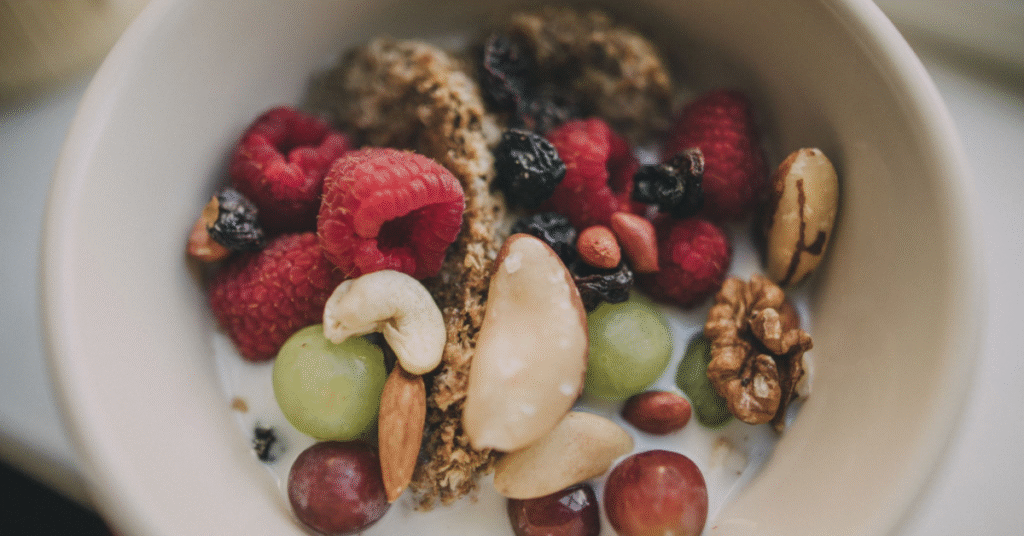 A healthy breakfast bowl containing yogurt, raspberries, grapes, cashews, almonds, and walnuts, illustrating a nutritious meal to fuel a productive morning.